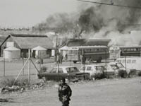 Burning building, with school busses and person in foreground, Mabopane.